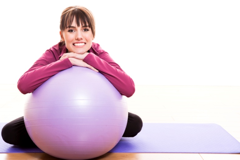 A woman leaning on an exercise ball.